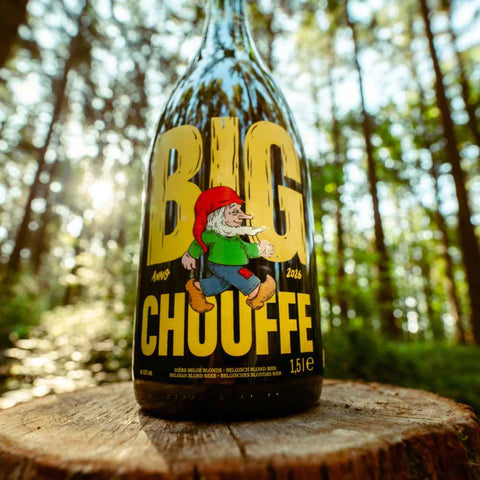 Frente da Garrafa cerveja belga Big Chouffe Magnum em cima de um tronco no meio da floresta