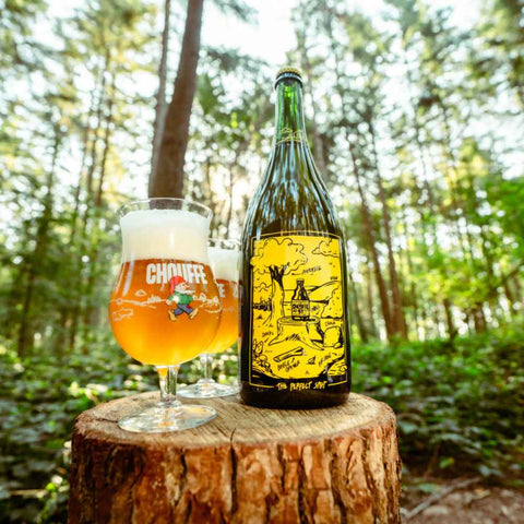 Garrafa cerveja belga Big Chouffe Magnum + 2 Copos em cima de um tronco no meio da floresta