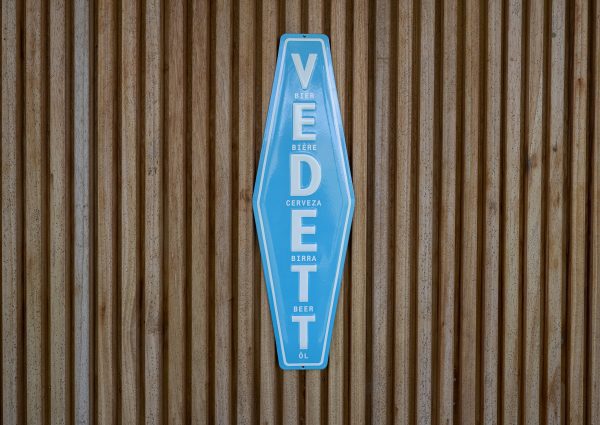 placa decorativa de parede esmaltada Vedett, azul e branca, sobre estrutura de ripas de madeira